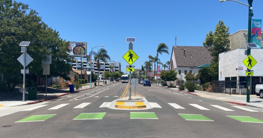 center view of a street with a bike lane and cross walk with safety lights. 