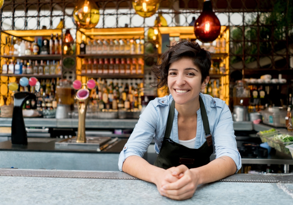 service worker in front of a bar, smiling leaning on the counter