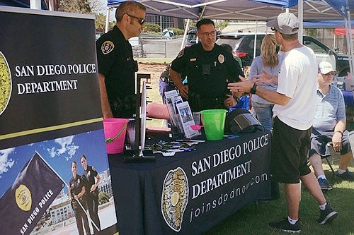 person speaking with two police staff at a SDPD booth