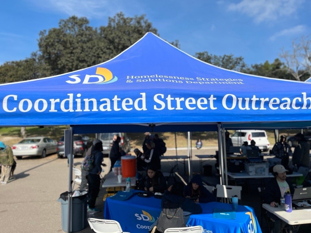 Coordinated Street Outreach City tent in a parking lot with tables set under the tent to help with outreach services.