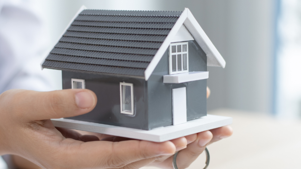 two hands holding a two story house mock with a key on their finger