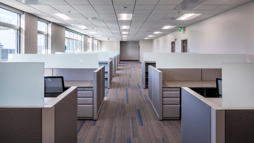 inside of an office with the aisle down the middle and two rows of cubicles lined up 